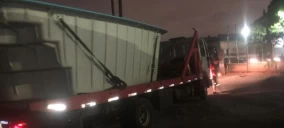 Guincho de plataforma transportando um contêiner em Campo Grande, à noite, estacionado na rua.