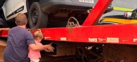 Guincho plataforma em Campo Grande, transportando veículo preto, com homem e criança ao lado.