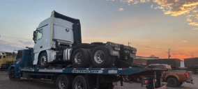 Guincho plataforma transportando caminhão branco em Floriano, ao entardecer, estacionado em área aberta.