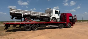Guincho plataforma vermelho transportando caminhão branco em área de terra em Floriano, PI.