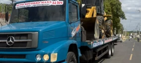 Guincho plataforma azul transportando uma retroescavadeira amarela em Floriano, estacionado na rua.