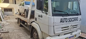 Guincho plataforma branco com um carro prata em cima, estacionado em área de serviço em São Mateus.