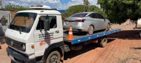 Guincho plataforma transportando um carro sedã prata em Palmas, com cone de sinalização na parte traseira.