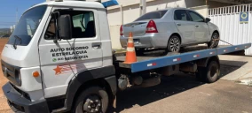 Guincho plataforma com carro prata estacionado na parte traseira, em Palmas, próximo a uma edificação.