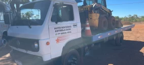 Guincho plataforma transportando uma retroescavadeira em Palmas, com cones de sinalização ao lado.
