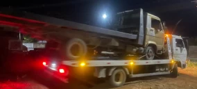 Guincho plataforma em Arcos transportando um caminhão pequeno, visível à noite com iluminação.