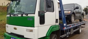 Guincho plataforma verde e branco transportando SUV preta em São Bento do Sul, estacionado em via pública.