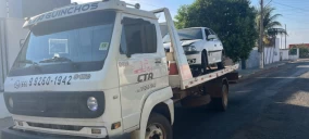 Guincho plataforma transportando um carro branco em Primavera do Leste, estacionado em uma rua.