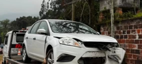 Guincho transportando um veículo branco com a frente danificada em Bom Princípio.