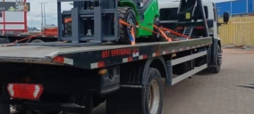 Guincho plataforma transportando um veículo verde, estacionado em Bom Princípio.