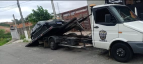 Guincho plataforma em Franco da Rocha transportando um veículo preto, estacionado em uma rua.