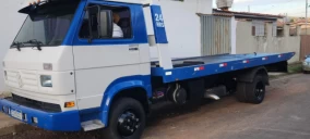Guincho plataforma estacionado em Novo Gama, com cabine azul e branca, sem veículo transportado visível.