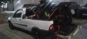 Caminhonete branca estacionada em Santo André, transportando uma moto amarrada na caçamba com cordas.