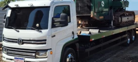 Guincho plataforma branco transportando uma máquina verde em Serra, ES.
