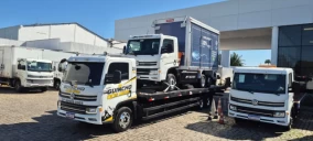 Guincho plataforma transportando um caminhão baú em Serra, com outros veículos estacionados ao fundo.