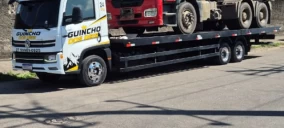 Guincho plataforma estacionado em rua, transportando caminhão vermelho.