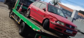 Guincho plataforma transportando um veículo Volkswagen vermelho, com danos visíveis, em Telêmaco Borba.