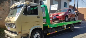 Guincho plataforma transportando um carro vermelho em Telêmaco Borba, estacionado em uma rua.