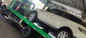 Guincho plataforma verde transportando um SUV branco em Telêmaco Borba, estacionado sob cobertura.