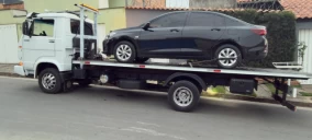 Guincho plataforma em Betim transportando um carro preto sobre a carroceria.