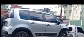 Guincho transportando um veículo prata, modelo Fiat Uno, estacionado em uma rua no Rio de Janeiro.