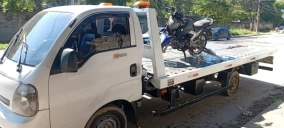 Guincho plataforma estacionado na rua, transportando uma motocicleta preta em Rio de Janeiro.