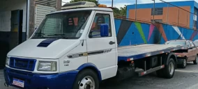 Guincho tipo plataforma estacionado em Suzano, com pintura branca e azul, sem veículo transportado visível.