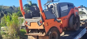 Guincho transportando um rolo compactador laranja em Carmo, com o veículo estacionado na plataforma.