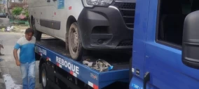 Guincho plataforma em Olinda transportando uma van branca, com um homem ao lado, em uma rua.