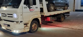 Guincho plataforma branco transportando um veículo cinza em Ibema, estacionado em uma rua iluminada.