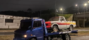 Guincho plataforma azul transportando uma caminhonete branca e vermelha em Viana, à noite.