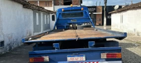 Guincho plataforma azul estacionado em rua de Sapeaçu, com carro não visível na parte traseira.