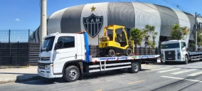 Guincho plataforma transportando uma empilhadeira amarela em Belo Horizonte, próximo a um estádio.