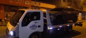 Guincho plataforma transportando um veículo preto em Praia Grande, à noite, estacionado em uma rua.