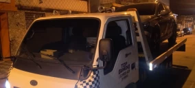 Guincho plataforma transportando um veículo preto em Praia Grande, com iluminação visível e ambiente noturno.