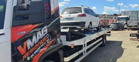Guincho plataforma em Teresina transportando um veículo branco, estacionado em área com outros carros ao fundo.