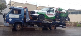 Guincho plataforma transportando um caminhão verde e branco em Goiânia, estacionado em uma rua.